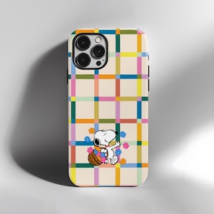 以下が含まれることがあります： 黄色、ピンク、青、緑のカラフルなチェック柄の携帯電話ケース。ケースには、花のバスケットを持っている漫画のスヌーピーのキャラクターが描かれています。このケースはスマートフォン用に設計されています。