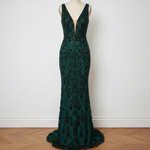 May include: A dark green, floor-length, sleeveless gown with a plunging V-neckline and intricate beading throughout.