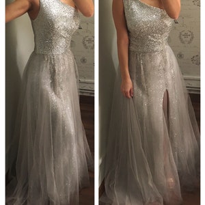 Model wearing a silver custom-made evening gown with a one-shoulder design, sparkling beaded bodice, and flowing tulle skirt featuring a thigh-high slit