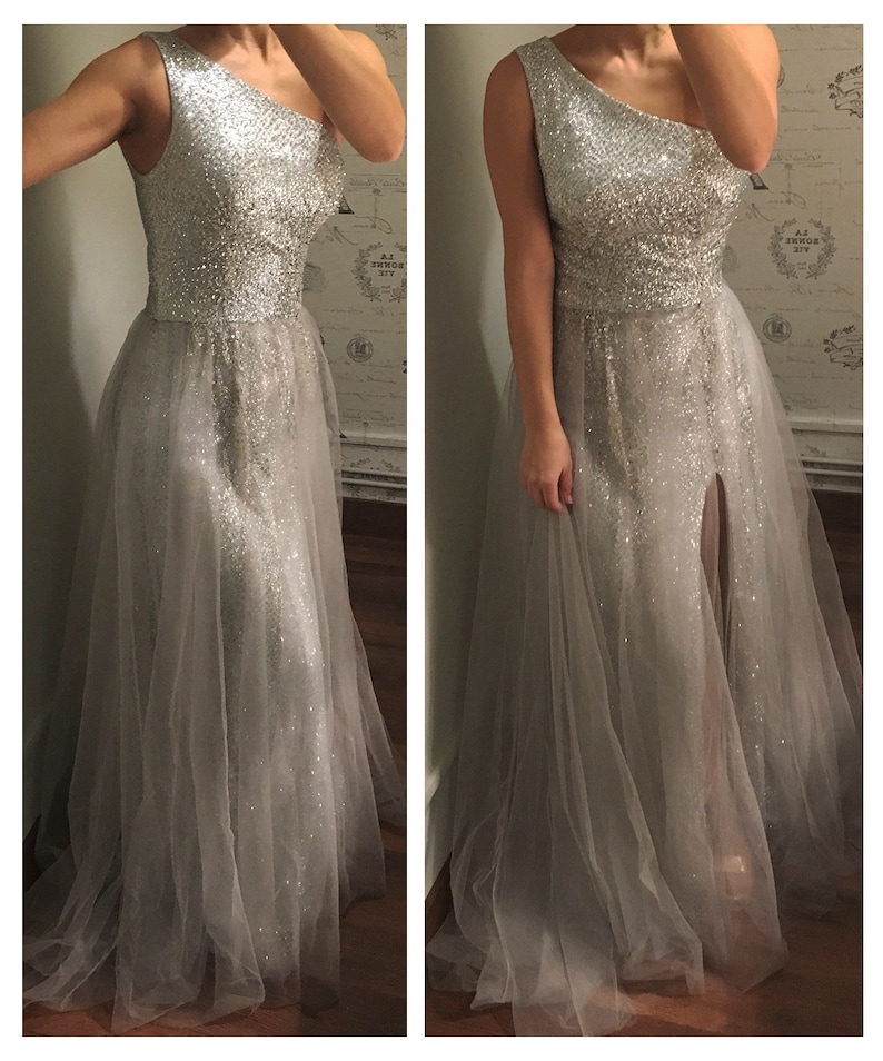 Model wearing a silver custom-made evening gown with a one-shoulder design, sparkling beaded bodice, and flowing tulle skirt featuring a thigh-high slit