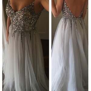 Model wearing a silver evening gown with a beaded bodice, spaghetti straps, and a flowing tulle skirt, featuring a deep V-back design