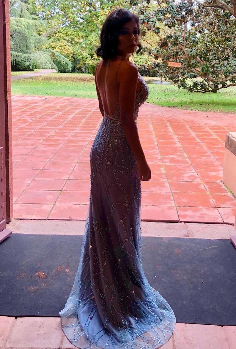May include: A woman wearing a long, light blue, beaded, backless gown with a mermaid silhouette.