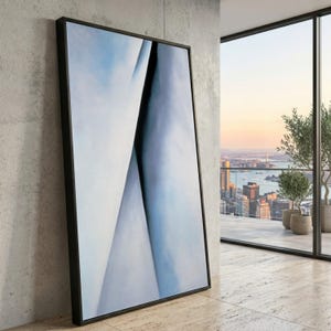 Puede incluir: Impresión artística abstracta en un marco negro. La obra presenta una mezcla de tonos azul claro y blanco, con una línea diagonal azul oscuro que crea una sensación de profundidad. El arte enmarcado está apoyado contra una pared de hormigón.