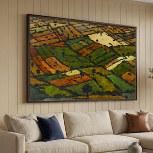 Könnte beinhalten: Großformatiges, gerahmtes abstraktes Landschaftsgemälde mit einem dunkelbraunen Rahmen. Das Kunstwerk zeigt ein Patchwork aus Feldern in Grün-, Orange- und Gelbtönen mit kleinen schwarzen Baumsilhouetten. Das Gemälde hängt über einem beigen Sofa.