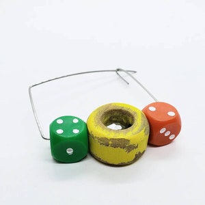 May include: A wire hoop with three wooden dice attached. The dice are painted green, yellow, and orange with white dots.