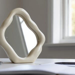 Peut inclure: Un miroir décoratif crème avec des bords ondulés est posé sur un bureau blanc. Un ordinateur portable et un stylo sont également sur le bureau. Sa forme unique en fait un élément de décoration élégant.