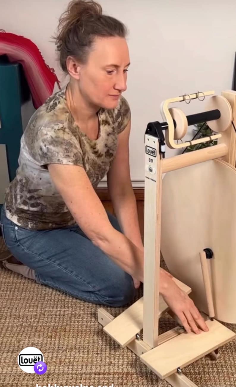May include: A light-colored wooden spinning wheel with a large circular wheel, a treadle base, and a flyer assembly. The frame features the brand name Lou&euml;t and the model S17 printed in black text. The device is constructed from light-toned wood.