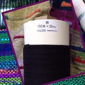 May include: A roll of black thread sits atop a colorful woven textile. The label on the thread spool reads "150本 x 30m" and includes Japanese text. The woven fabric features a variety of colors, including green, purple, and orange.