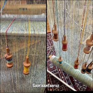 May include: A loom with vertical threads and several wooden spools holding colorful yarn. The spools are suspended, ready for weaving. The text "Saorisantacruz" is visible in the bottom center.