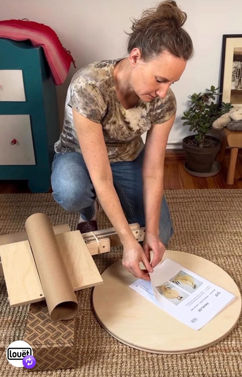 May include: A light-colored wooden circular base and a wooden assembly with a cardboard tube, accompanied by a printed instruction manual labeled S17 EN/NL/DE, featuring diagrams of a spinning wheel component on a textured beige rug.