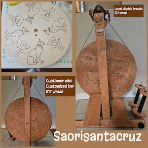 Puede incluir: Un torno de hilar Louet S17 de doble pedal con una rueda de madera personalizada que presenta un patr&oacute;n repetitivo de gatos y flores. La rueda est&aacute; hecha de madera natural con un acabado marr&oacute;n c&aacute;lido. El texto "Louet S17" es visible en el lateral de la rueda.