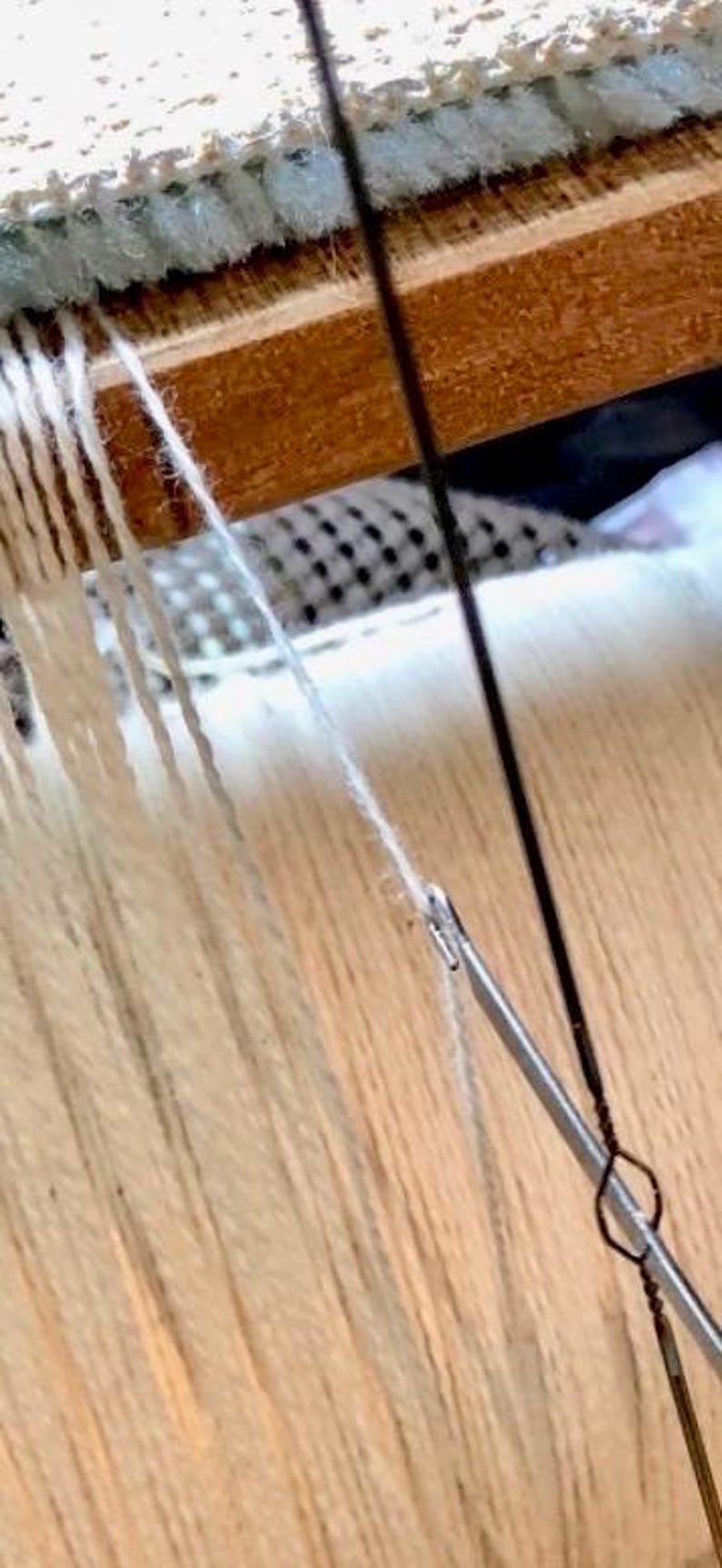 May include: Close-up of a weaving project in progress. The image shows white yarn threads being woven on a wooden loom. A metal needle is used to manipulate the threads, creating a textured fabric.