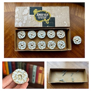 May include: A set of eleven round cabinet knobs with a white floral relief pattern and a gold-tone center, housed in a cardboard box labeled Kwee-ver ware. The set includes metal mounting screws, and each knob features a circular design.
