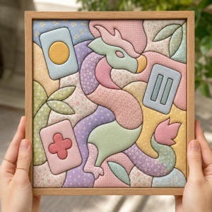 Op de afbeelding: Een vierkant ingelijst wandkunstwerk met een gewatteerde stoffen draak in pasteltinten zoals roze, groen en paars. De draak is omringd door abstracte vormen, waaronder rechthoekige kaarten met een gele cirkel, een roze bloem en twee verticale lijnen.