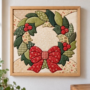 May include: A square wall art piece featuring a fabric-pieced wreath design in a light wooden frame. The wreath is composed of various green and cream patterned fabric leaves with clusters of red berries and a large red gingham bow at the base.