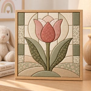 Op de afbeelding: Een vierkant wandkunstwerk met een stoffen tulpenontwerp in tinten oudroze, saliegroen en crème. Het kunstwerk is opgebouwd uit gewatteerde stoffen segmenten in een geometrisch patroon en gevat in een lichthouten lijst.