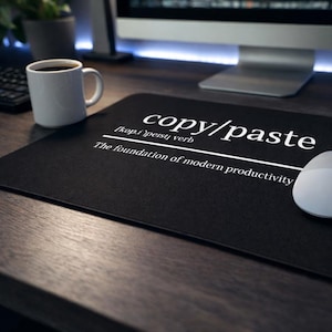 May include: Black rectangular mouse mat with the words "copy/paste" in white, along with a definition. A white computer mouse is on the right side of the mat. A white coffee mug sits on the left.
