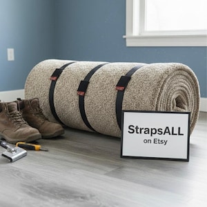 May include: A rolled-up beige carpet secured with black straps. The carpet is next to a pair of brown boots, a carpet knife, and a sign that reads "StrapsALL on Etsy". The background is a blue wall and a window.