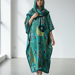 Puede incluir: Un caft&aacute;n con capucha de color turquesa con un estampado de tem&aacute;tica natural con &aacute;rboles y flores. El caft&aacute;n tiene un borde turquesa oscuro y se combina con una bufanda a juego. La persona lleva zapatillas blancas.
