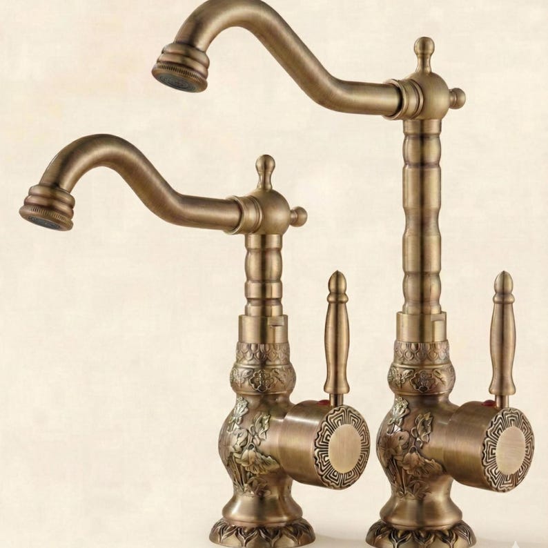 May include: Two antique-style bronze faucets. The faucets have curved spouts and ornate detailing on the base and handles. The handles are lever-style. The finish is a warm, aged bronze color.