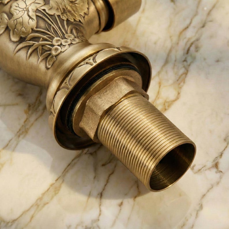 May include: Close-up of a vintage-style faucet with an antique brass finish. The faucet features intricate floral and leaf detailing on the spout and a threaded base. The design suggests a classic or traditional bathroom fixture.