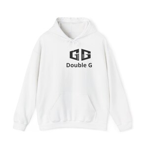Puede incluir: Sudadera con capucha blanca con bolsillo delantero y cordón. El gráfico negro en la parte delantera presenta el texto "Double G" debajo de un logotipo estilizado. El logotipo incluye las palabras "GOOD GOD" dentro del diseño.