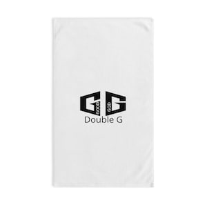 Puede incluir: Toalla rectangular blanca con un logotipo Double G negro. El logotipo presenta dos G estilizadas, con "GOOD" y "GOD" impresos verticalmente dentro de cada G. Debajo del logotipo está el texto "Double G".