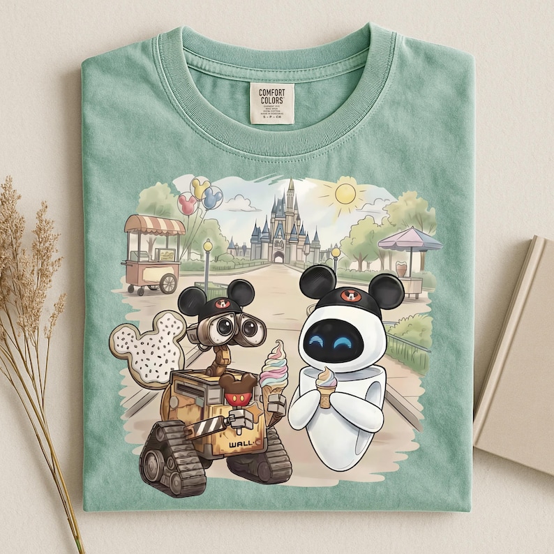 Puede incluir: Camiseta verde menta Comfort Colors con un gr&aacute;fico colorido de WALL-E y EVE comiendo helado frente a un castillo. El dise&ntilde;o incluye donuts y sombreros tem&aacute;ticos de Mickey Mouse, y un puesto de comida.