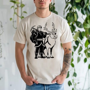K&ouml;nnte beinhalten: Beiges T-Shirt mit einer schwarz-wei&szlig;en Grafik eines Charakters mit einer Spitzhacke und einem Rentier. Der Charakter tr&auml;gt ein Winteroutfit und steht neben dem Rentier. Das Rentier hat ein Geschirr.