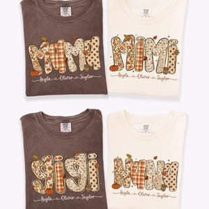 May include: Four short-sleeve t-shirts in brown and cream colors. Each shirt features a large graphic with the words MAMA, MIMI, GIGI, or NANA in a fall-themed pattern, including pumpkins, leaves, and plaid. Below each word are the names Layla, Oliver, and Taylor.
