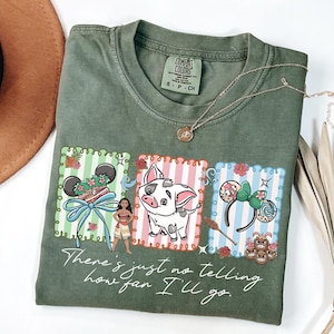 May include: An olive green t-shirt featuring a graphic print of Moana, Pua the pig, and two pairs of character-themed mouse ears. The text "There's just no telling how far I'll go" is printed in white script below the colorful rectangular illustrations.