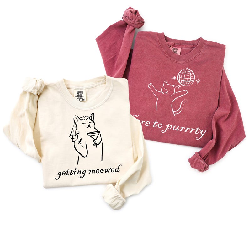 May include: Two long-sleeved shirts. One is cream-colored with a black graphic of a llama holding a martini glass, with the text "getting meowed". The other is maroon with a white cat graphic and the text "here to purrrty".