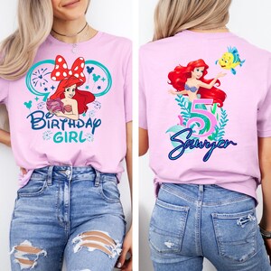May include: A light purple t-shirt featuring a graphic of Ariel from The Little Mermaid with the text "Birthday Girl" on the front. The back of the shirt has Ariel, the number 5, and the name "Sawyer".