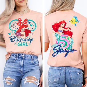 May include: Peach-colored t-shirt featuring a front graphic of a mermaid with the text "Birthday Girl". The back of the shirt displays a mermaid, the number 5, and the name "Sawyer".