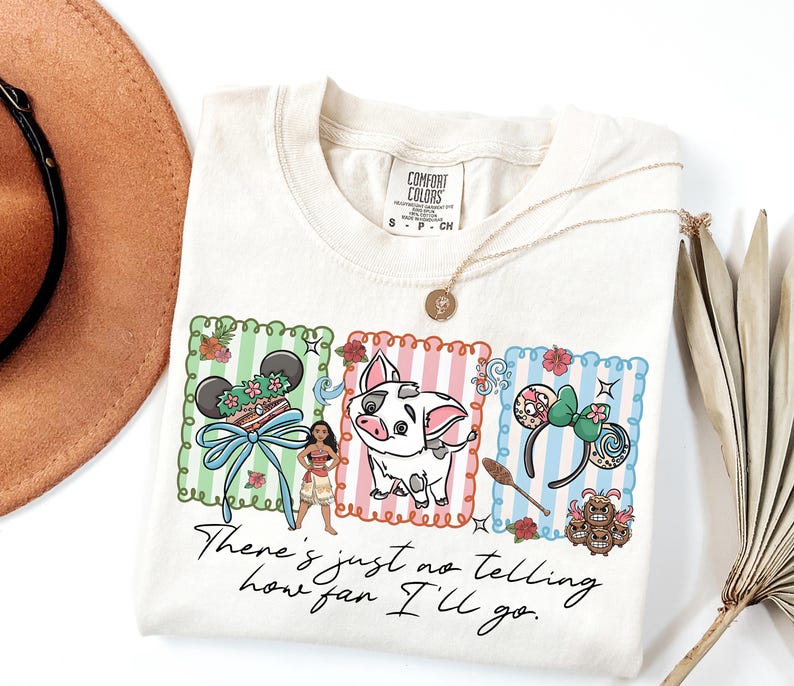 May include: A cream-colored t-shirt featuring a graphic with three vertical striped panels in green, pink, and blue. The design includes a character, a pig, mouse ears, and the text "There's just no telling how far I'll go." The shirt has a Comfort Colors label.