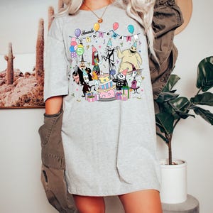 May include: A light grey t-shirt with a colourful graphic of characters from The Nightmare Before Christmas celebrating a birthday. The text "Amanda Birthday" is displayed above the characters, with a number "5" on a balloon.
