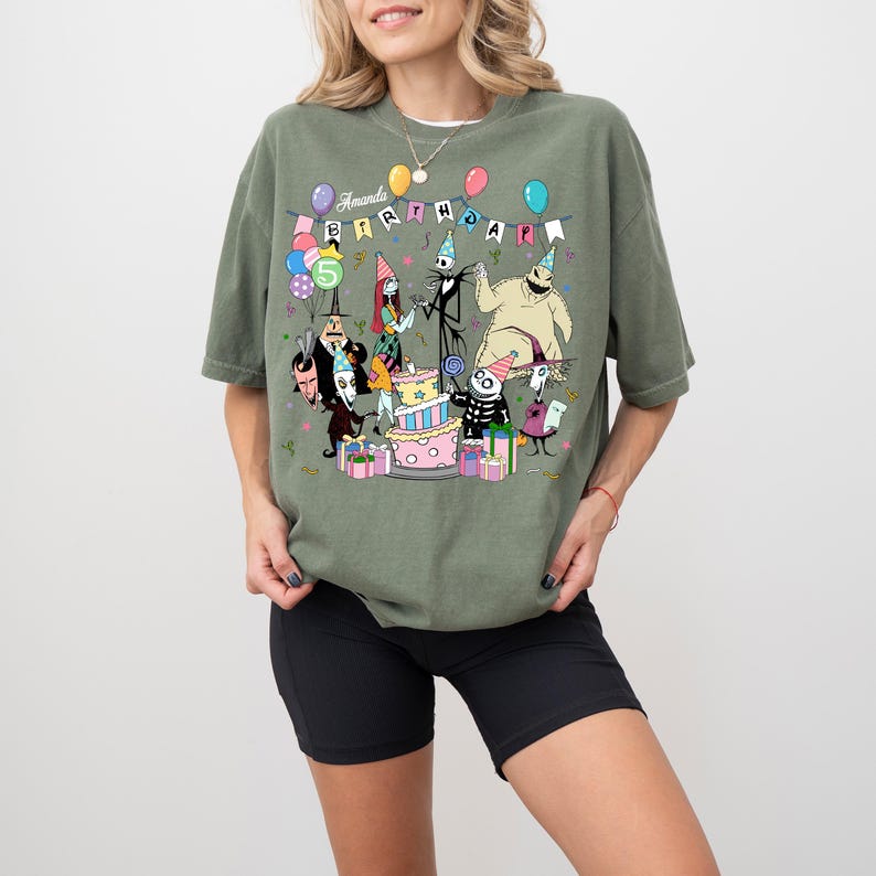 May include: Olive green t-shirt with a colourful graphic of characters from The Nightmare Before Christmas celebrating a birthday. The text "Amanda Birthday" is displayed above the characters. Balloons and a cake are also included in the design.