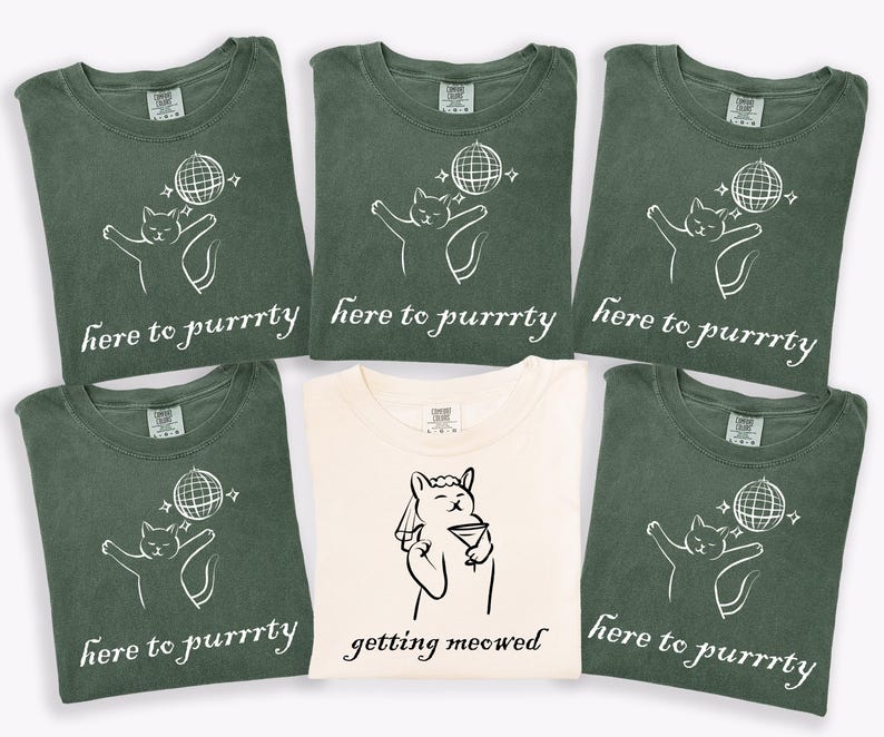 May include: A collection of green and cream-colored t-shirts. Most shirts feature a white graphic of a cat with a disco ball and the text "here to purrrty." One cream shirt has a cat with a martini and the text "getting meowed."