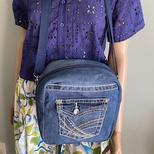 Puede incluir: Bolso cruzado de mezclilla con un bolsillo delantero con costuras decorativas y un botón plateado. El bolso tiene cierre de cremallera y una correa azul. El bolso está hecho de mezclilla azul.