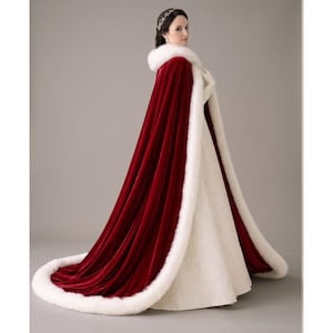 May include: A long, flowing red velvet cape with a white faux fur trim and hood. The cape is paired with a white dress. The elegant design is suitable for special occasions, such as weddings or formal events.