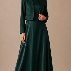 May include: A dark emerald green ensemble consisting of a floor-length, sleeveless maxi dress with a high neckline and a matching cropped blazer with long sleeves, a notched lapel, and a single button closure, paired with beige high-heeled pumps.