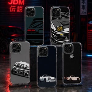 May include: Five clear phone cases featuring JDM car illustrations. One shows a rear view of a dark car, another a front view with yellow headlights, one a drifting car, one a white sports car, and one a white car with the Japanese kanji for dream.