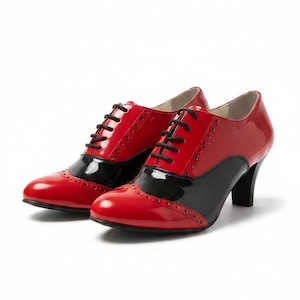 Könnte beinhalten: Paar rote und schwarze Lackleder-Oxfords mit Absatz und schwarzen Schnürsenkeln. Die Schuhe haben ein klassisches Flügelspitzendesign mit runder Spitze und kleinem Absatz. Die Schuhe sind vor weißem Hintergrund.