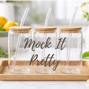 May include: Three clear glass drinking jars with bamboo lids and glass straws, arranged on a wooden tray. The text "Mock It Pretty" is written on the jars. Sliced oranges and lemons are in the foreground.