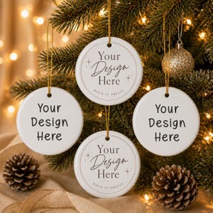 May include: Four round white ceramic ornaments hanging from gold strings. Two ornaments feature the black text 'Your Design Here' in a simple font, while the other two feature the text 'Your Design Here' in a script font with star accents.