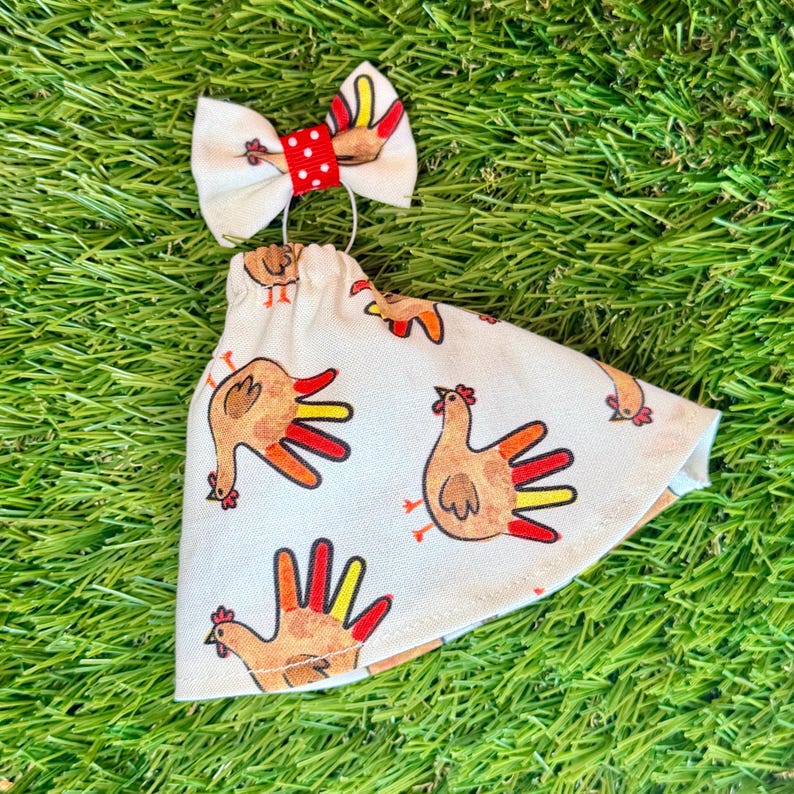 May include: A cream-colored fabric cone-shaped accessory featuring a repeating print of brown chickens with red and yellow tail feathers. The top is adorned with a small cream bow featuring a central red band with white polka dots.