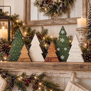 May include: A set of six decorative wooden Christmas tree figurines in varying sizes and finishes. The collection includes two green trees with white snowflake and dot patterns, two natural wood trees, one brown stained tree, and one white tree.