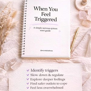 May include: A spiral-bound workbook titled "When You Feel Triggered" with the subtitle "A simple nervous system reset guide." The cover is white with purple text. A list of steps to identify triggers and cope is below the book. A gold pen and crystals are next to the book.