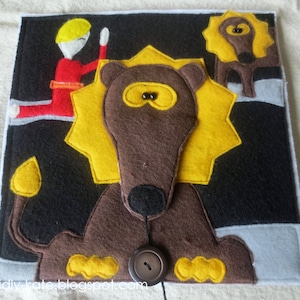 May include: A felt book page with a brown lion with a yellow mane and a button nose. The lion is on a black background with a white border. There is a smaller yellow lion in the upper right corner of the page.