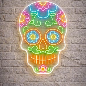 May include: A colorful neon sign in the shape of a sugar skull, with floral designs. The skull features bright neon colors including pink, blue, green, and orange. The sign is mounted on a white brick wall.